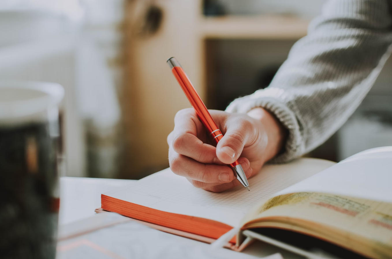 Student writing in a book with Red Pen